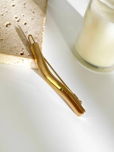 Detailed view of a golden irregular geometric hair clip on a minimalist stone surface