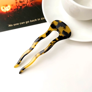 Detailed view of U-shaped tortoiseshell hair pin with amber texture on a white table