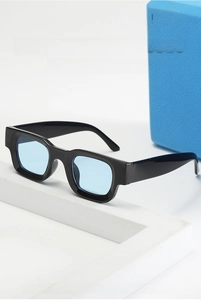 Detail einer schwarzen eckigen Sonnenbrille mit hellblauen Gläsern auf Steinfundament