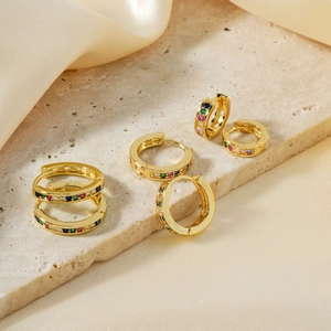 Eleganti orecchini dorati con pietre di zircone colorate su una superficie di pietra