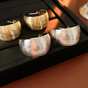 Detail of wide C-shaped earrings in gold and silver with brushed metal texture finish