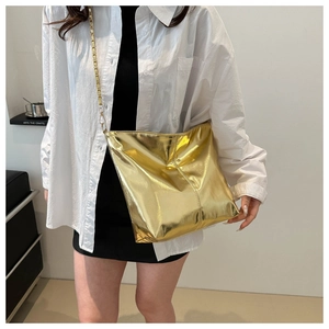 Close-up of a stylish gold metallic bucket bag with a chain strap worn by a model