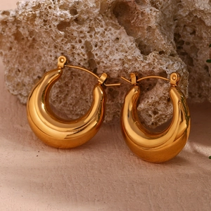 Detailed close-up of chunky gold hollow U-shaped hoop earrings on a textured stone surface