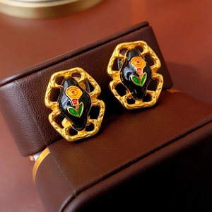 Macro detail of vintage gold earrings with black enamel and red green floral patterns