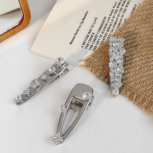 Three elegant silver hair clips with shimmering transparent zircons on a white surface