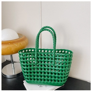 Close-up of a green hollow woven plastic tote bag styled on books with an orange lamp