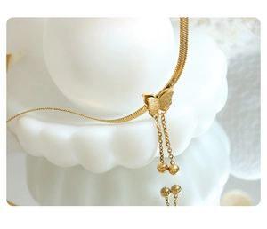 Detail showing gold butterfly pendant with tassel beads on a flat snake chain