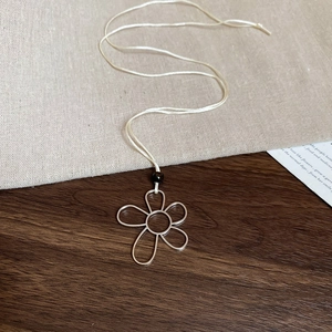 Detail of silver flower wire pendant on cream cord over rustic linen and wood