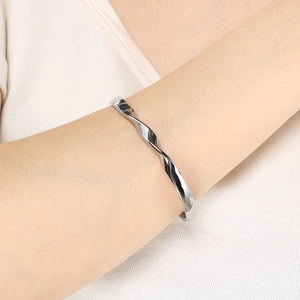 Detail of a minimalist silver wavy twisted bangle worn on a wrist with neutral background