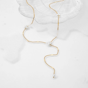 Elegant gold Y-shaped necklace with white pearls and square charms on a glass shell