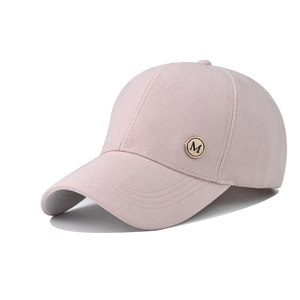 Detail of light pink baseball cap featuring a round gold M metal badge and ribbed texture