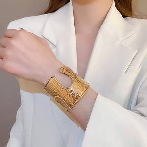 Detail of wide gold hammered texture cuff bracelet on model with white blazer