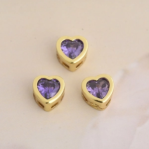 Detailed view of heart-shaped gold plated copper charms with purple cubic zirconia crystals