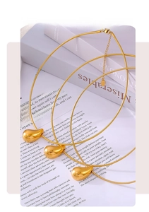 Detailed close-up of a gold teardrop pendant with a sleek snake chain on a book