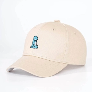 Close-up of the detailed teal dinosaur embroidery on a beige cotton baseball cap texture