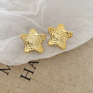 Macro detail of star-shaped golden stud earrings featuring a vintage textured grid pattern