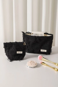 Detail of black cotton linen cosmetic bag with frayed edges and golden petal zipper pull
