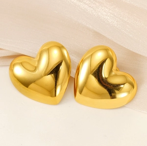 Macro shot of 18k gold heart-shaped stud earrings on soft pearl silk fabric background