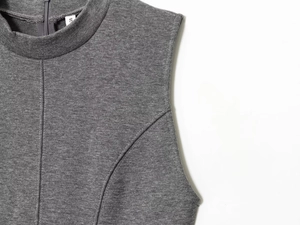 Detail van een grijze mouwloze top met hoge hals, naden en ritssluiting afwerking