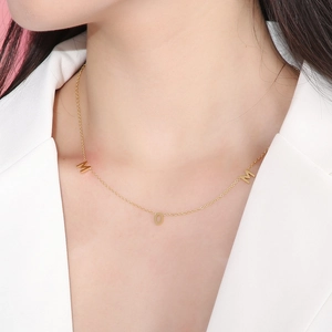 Macro detail of gold-plated MOM letter necklace pendant worn by a model in white blazer