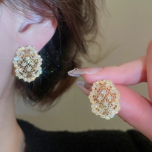 Gros plan de boucles d'oreilles fleurs dorées ajourées serties de zircons blancs