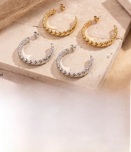 Detailed view of gold and silver C-shape twisted hoop earrings on stone background