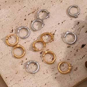 Detailed close-up of gold and silver hoop earrings with square zircon on stone background