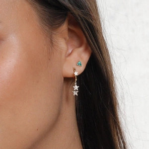 Close-up of sparkling star-shaped earrings and green stud on model ear for display