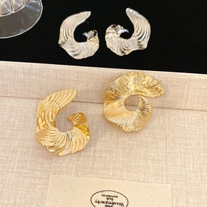 Macro detail of irregular C-shaped gold and silver earrings with spiral texture