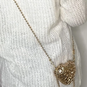 Detail of a gold heart-shaped hollow metal bag with a beaded chain on a white knit sweater