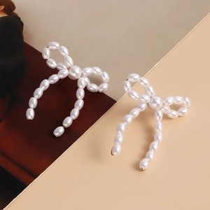Detail of elegant handmade pearl bow earrings with gold-tone hardware on aesthetic background