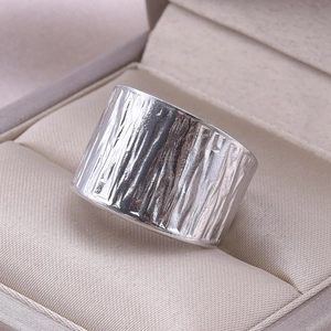Detail of wide silver ring showing unique bark texture on a silk jewelry box cushion