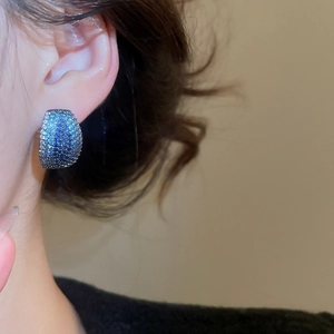 Close-up of sparkling blue zircon pavé C-shaped silver earrings on model ear