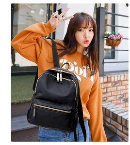 Detail of black oxford nylon backpack with gold zippers worn by model in orange hoodie