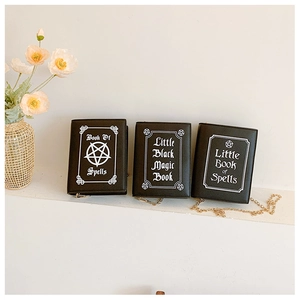 Detailed view of three black book-shaped crossbody bags with mystical spell book prints