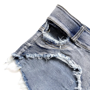 Dettaglio di pantaloncini di jeans blu con orli sfilacciati e trame di tessuto logoro