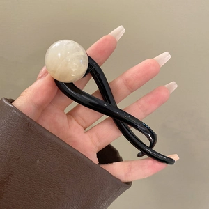 Detail of a black twisted knot hair clip with a cream resin bead for French chic styling