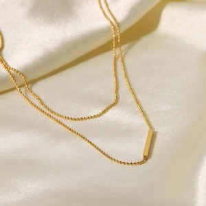 Macro shot of 18K gold plated bead chain with minimalist T-bar pendant on white silk