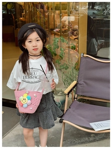 Close-up of pink woven bucket bag with rainbow floral charm on child outfit