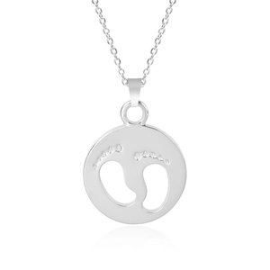 Macro detail of silver baby footprints cutout on a polished stainless steel round pendant