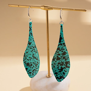 Detailed close-up of teal leaf-shaped earrings with black splatter pattern on gold display