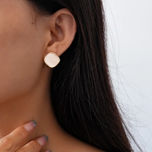 Detail of square gold-rimmed earring with white spiral enamel on a model ear