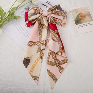 Close-up of printed satin bow hair clip with gold chain patterns on a flat lay fabric