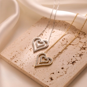 Luxurious gold and silver zircon heart pendant necklaces displayed on a beige stone base