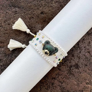 Close-up of hand-woven bear bracelet with green crystals and stylish white tassels