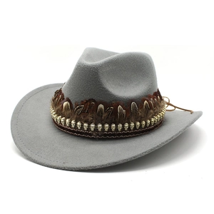 Detail of grey felt cowboy hat featuring golden skull trim and a dark brown feather