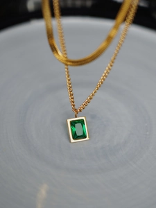 Macro detail of a double-layered gold snake chain with vintage emerald zircon pendant