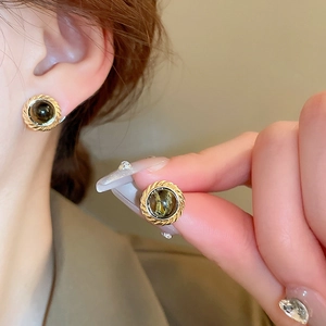 Close-up of vintage round tiger eye earrings with golden twisted metal frame worn by model