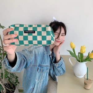 Green and beige checkered corduroy pouch held by a model in a cozy lifestyle setting