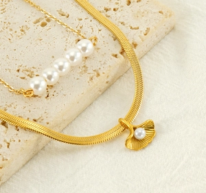 Close-up of golden ginkgo leaf pendant and pearl layered necklaces on stone texture